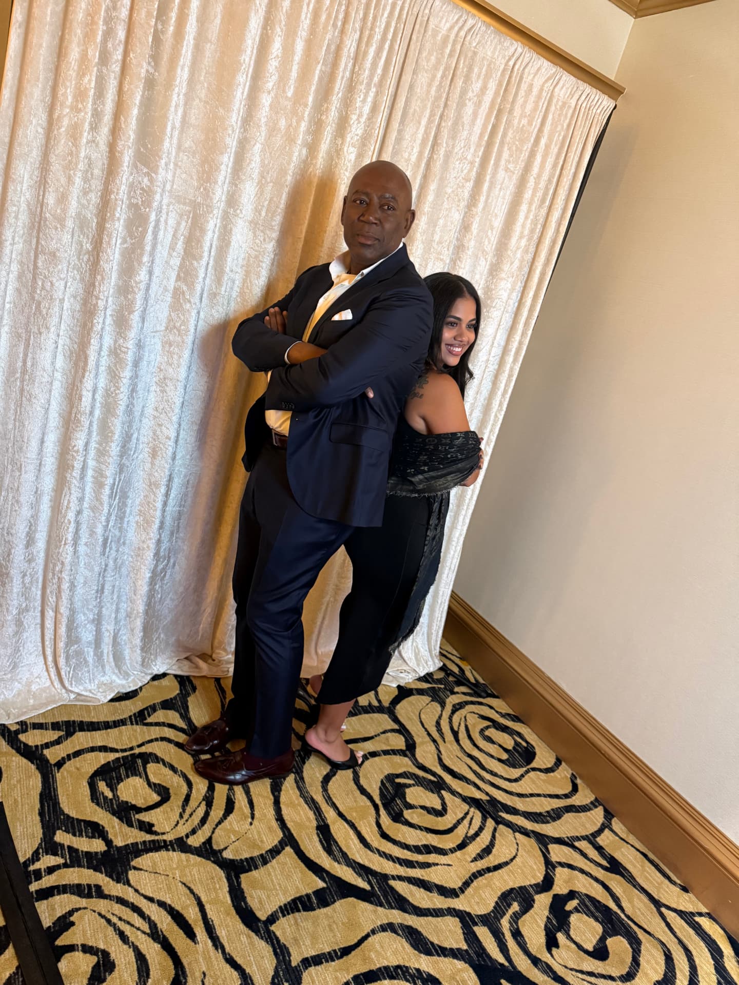 Two guests posing back to back in front of an ivory velvet drape