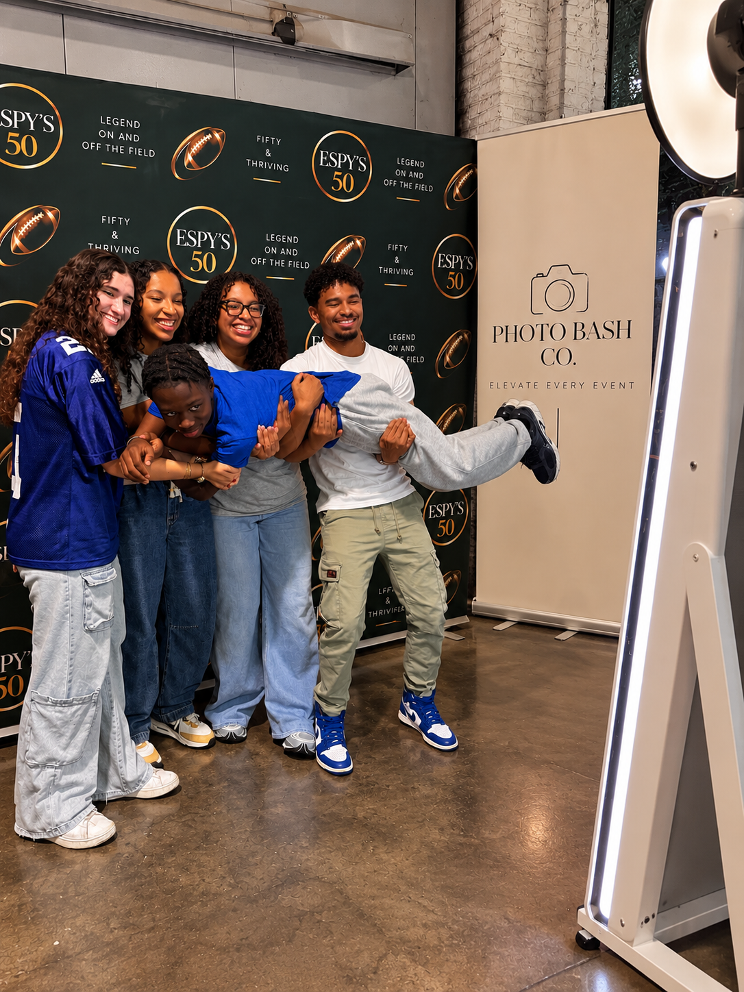Friends laughing and lifting a guest in front of the Photo Bash Co. mirror booth